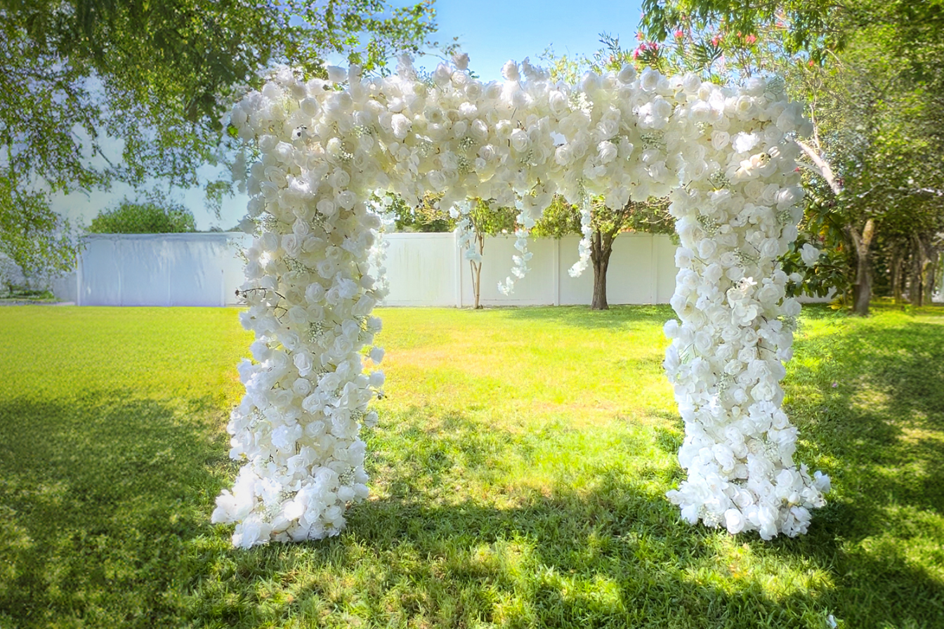 There is a white rose arch in the grassy field.